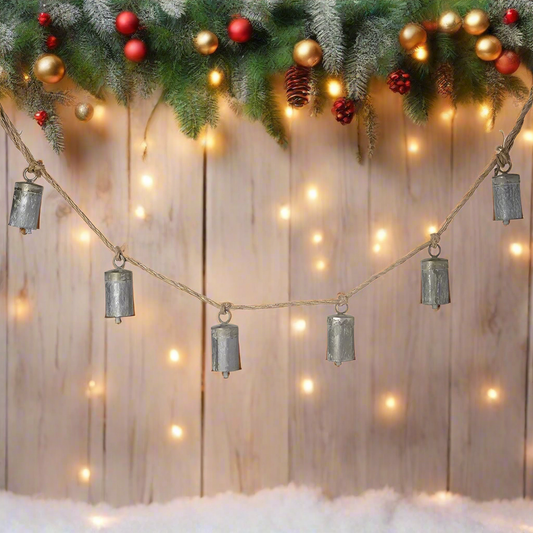 A string of matt silver cow bells with a rustic finish, hung on a jute rope.