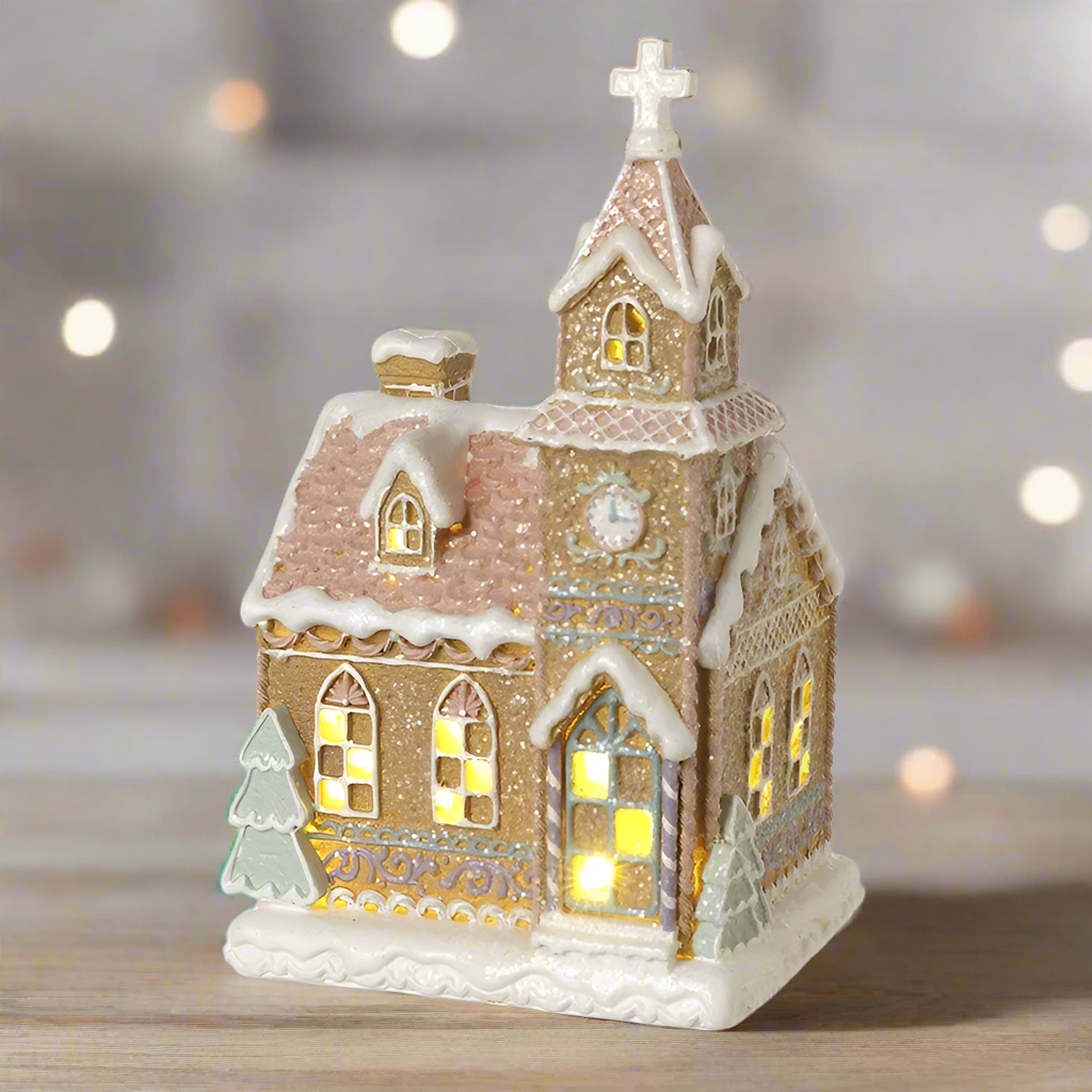 A resin ornament in the shape of a snowy gingerbread church with multicolored patterns and gold accents.