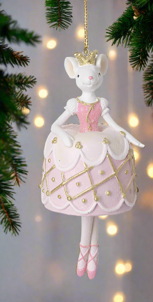 A decorative ballerina mouse hanging ornament in pink and gold attire with a crown, posed on one leg with a Christmas tree in the background.