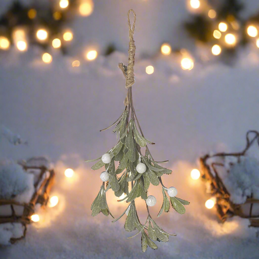 Hanging mistletoe decoration with white berries against a snowy background with lights.