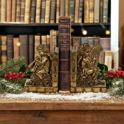 Two vintage gold cherub bookends with one bookend showing an angel playing a musical instrument and the other bookend showing an angel holding a harp. Both bookends are placed on a white surface with a background of books.