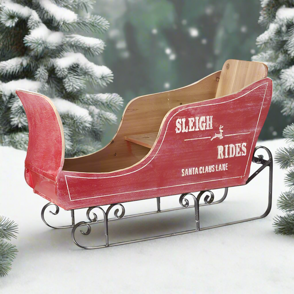 A rustic style wooden Christmas sleigh decoration with red and natural wood colors, featuring metal runners and the text 'SLEIGH RIDES' on the side.