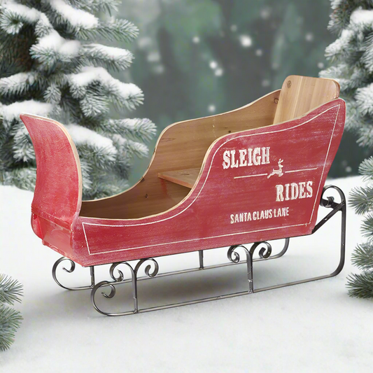 A rustic style wooden Christmas sleigh decoration with red and natural wood colors, featuring metal runners and the text 'SLEIGH RIDES' on the side.