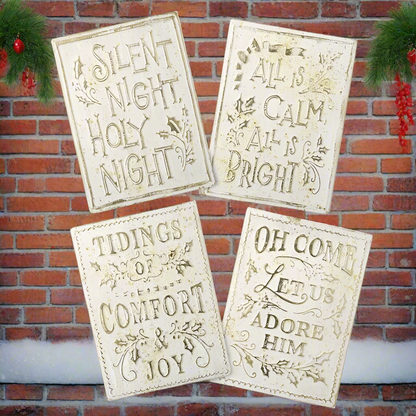 Four Christmas-themed signs with decorative text against a brick wall.