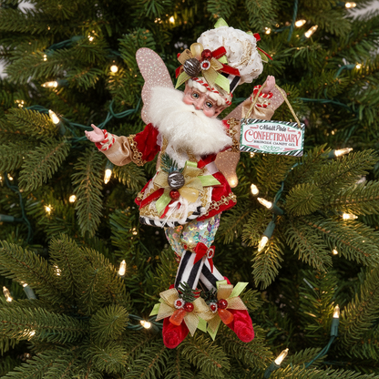 A decorative figure of a Santa fairy with wings, dressed in a festive red and green outfit, holding a sign, and adorned with magical jewels.