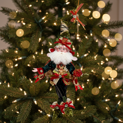 A vintage-style Christmas decoration featuring a fairy with a green hat and red bow, multicolored coat, and a wreath-decorated hat tip.