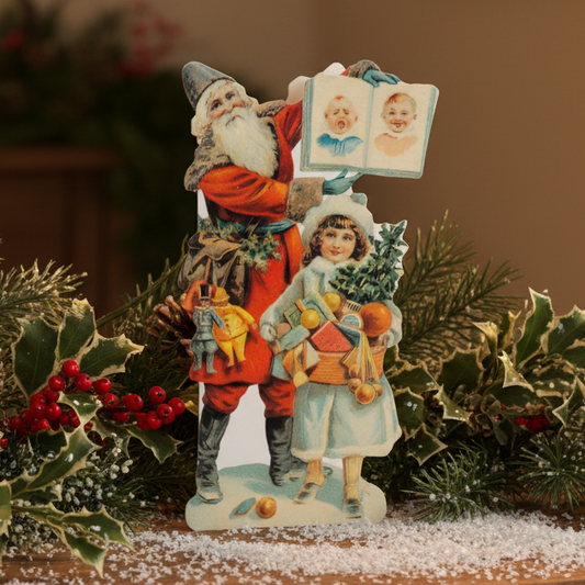 A greeting card featuring an illustration of Father Christmas holding a child, with a decorated Christmas tree and gifts in the background. The card is in a vintage style and appears to be embossed.