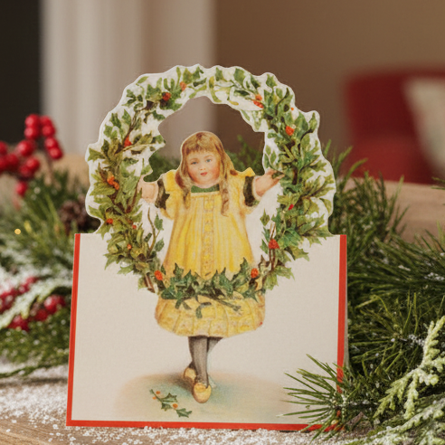 A Christmas card featuring a Victorian-inspired illustration of a girl with a holly wreath. The card is blank, with an envelope included.
