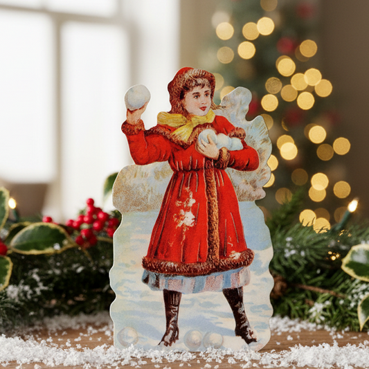 A Christmas card featuring a Victorian-inspired illustration of a girl in a red coat holding a snowball, with snowflakes and an envelope included.
