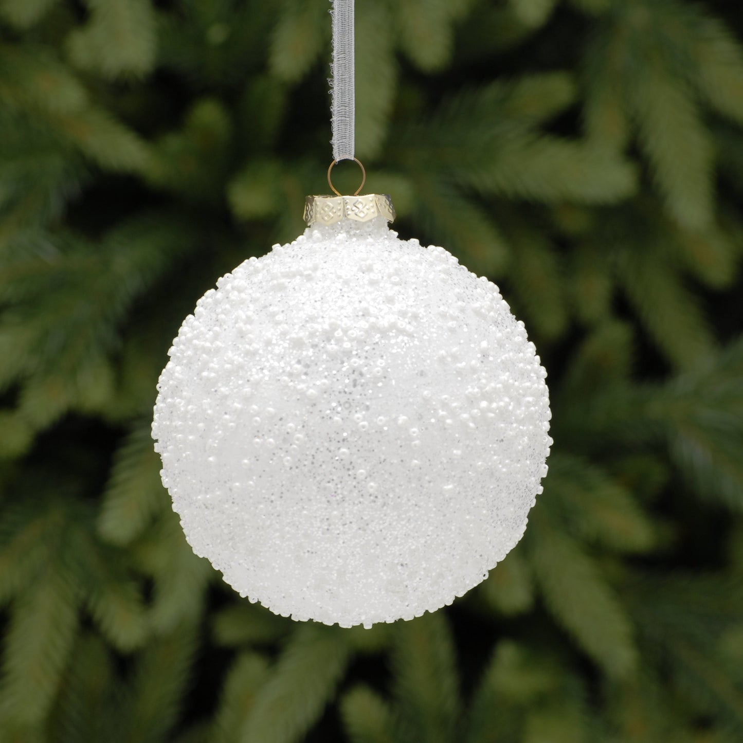 White textured Christmas ornament hanging against a green pine tree background