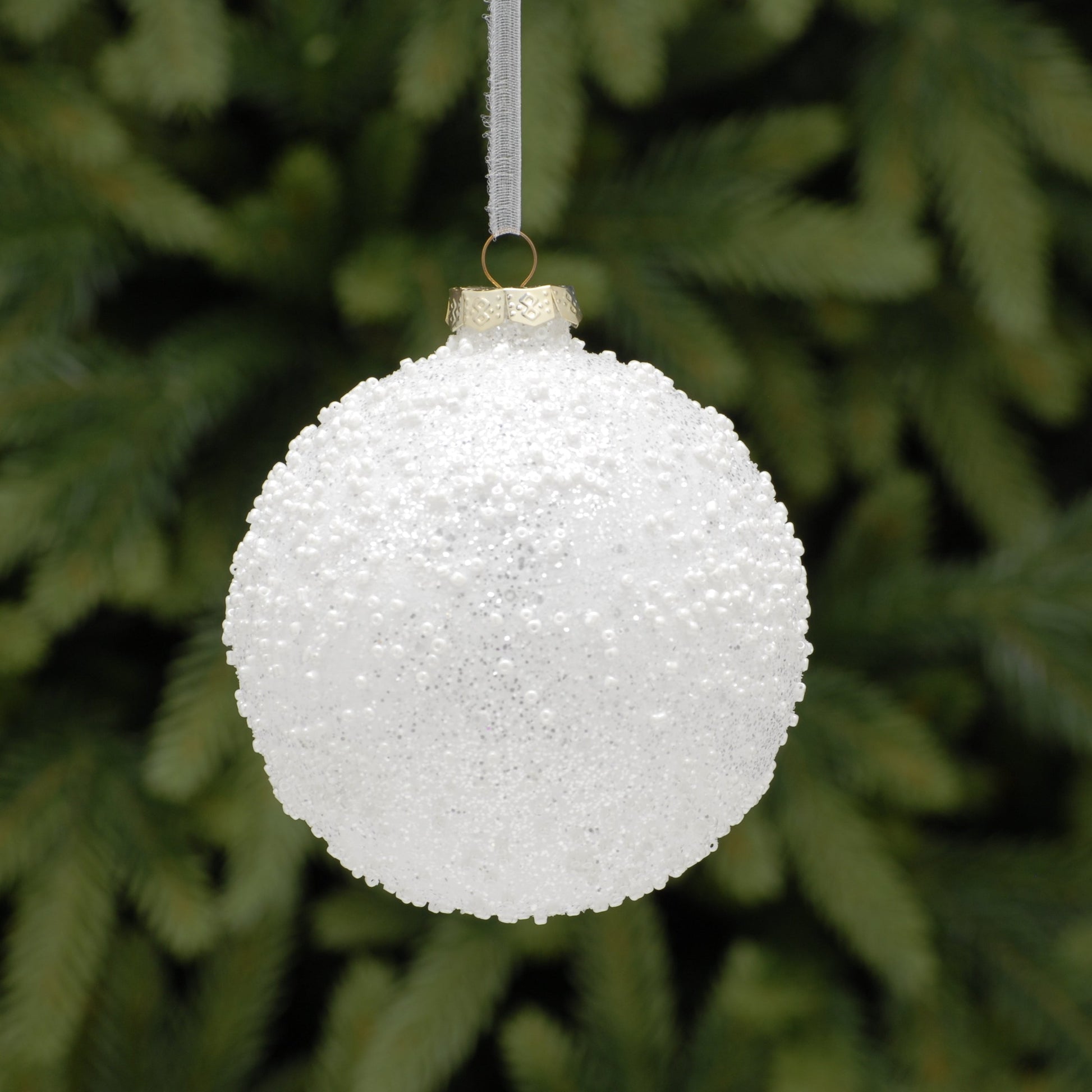 White textured Christmas ornament hanging against a green pine tree background