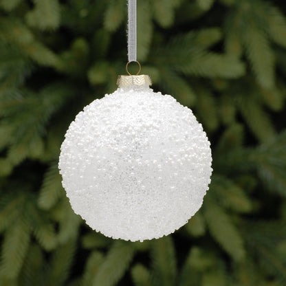 White textured Christmas ornament hanging against a green pine tree background