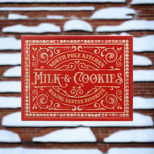 A red metal Christmas wall sign that reads 'NORTH POLE KITCHEN MILK & COOKIES MAKING SANTA'S FAVORITE SINCE 1982' with decorative elements and a white border.
