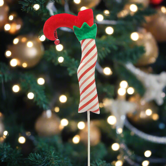 A festive Christmas elf leg pick decoration with a red shoe on a striped white and red stick, with green holly on top.
