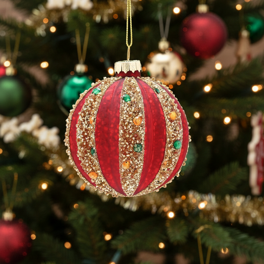 Decorative red and gold Christmas ornament with gemstones on a blurred green tree background