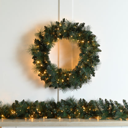 A Pre Lit Firefly Christmas Wreath with green pine needles and warm white LED lights, displayed indoors.