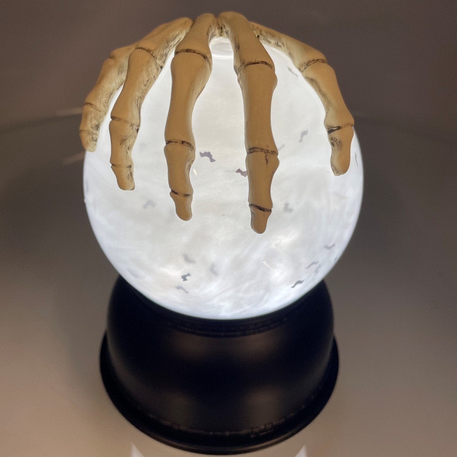 Glowing snow globe with a hand-like object on top against a dark background