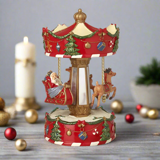 A decorative Santa Sleigh Spinning Christmas Merry Go Round with Santa and reindeer figures, decorated with red and green accents on a 25cm tall ornately decorated base.