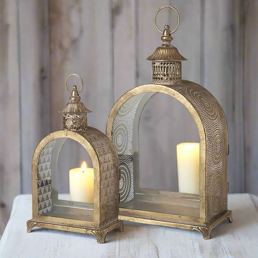 A set of two gold metal lanterns with glass panels, featuring intricate patterns and designs on the lantern bodies.