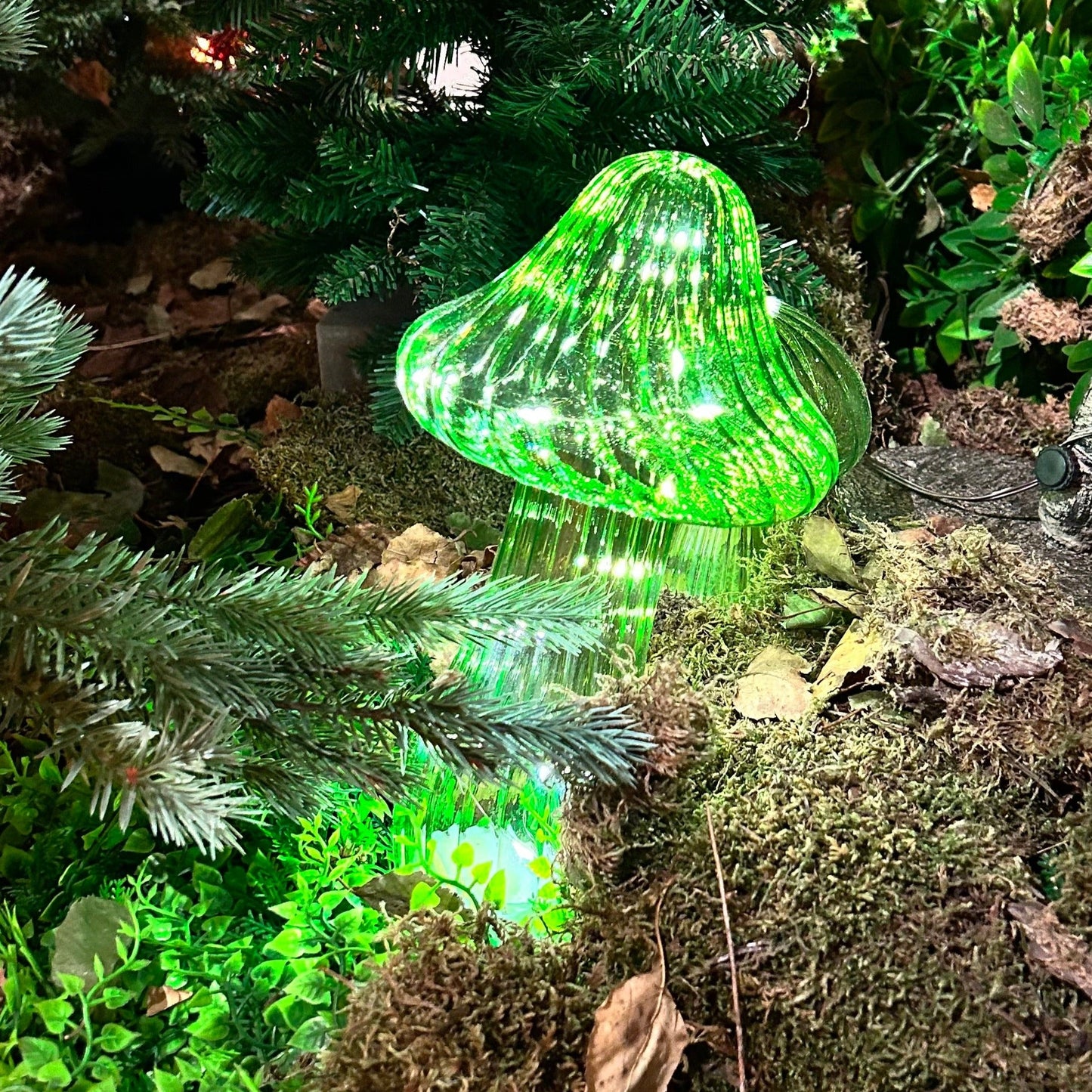 Green LED mushroom light on a forest floor with moss and leaves