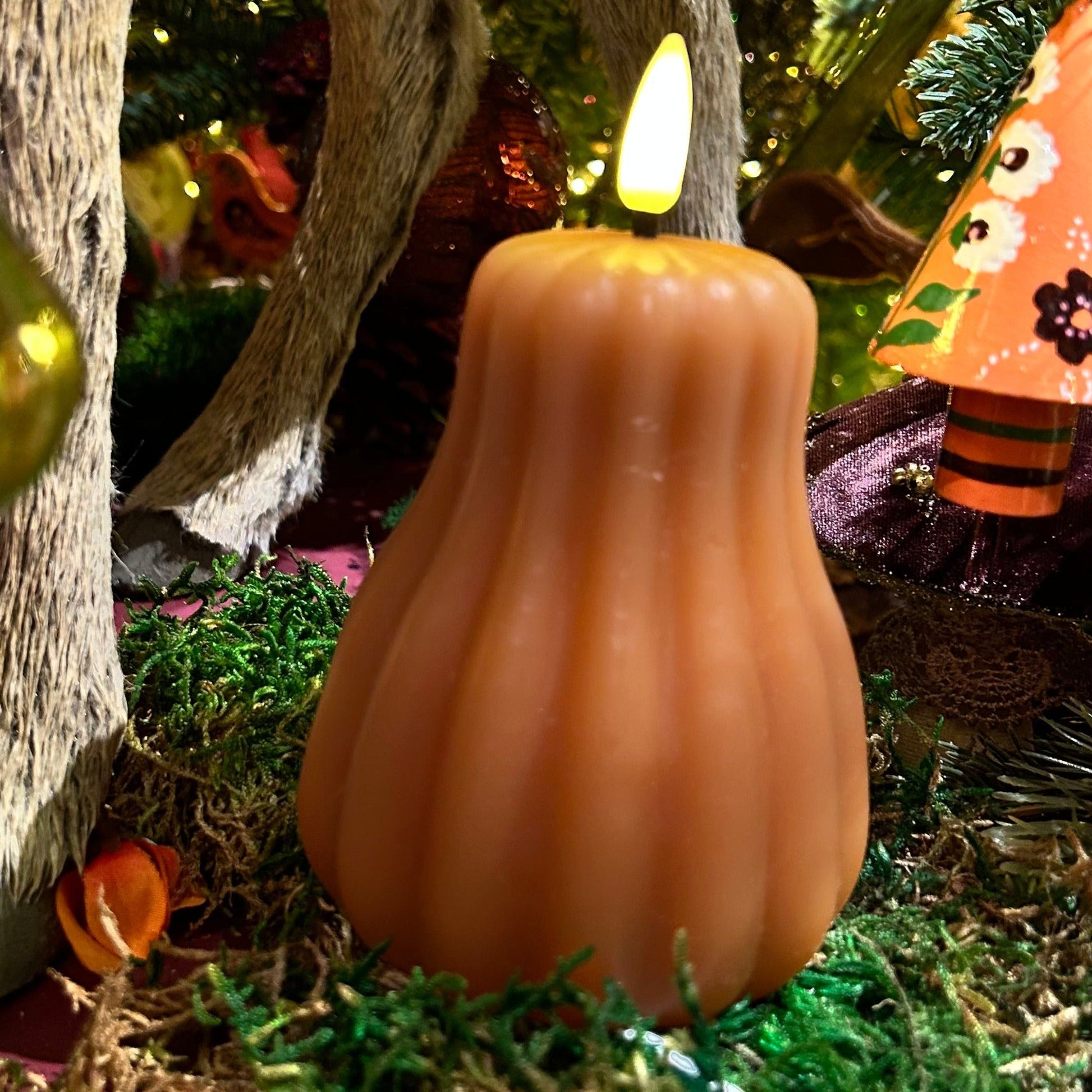 Pumpkin-shaped candle with a lit wick in a festive setting with decorations.