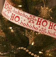 Decorated Christmas tree with 'HO HO HO' ribbon and ornaments against a blurred background