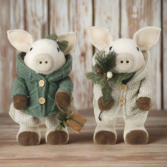 Two plush pig ornaments dressed in festive clothing, one in green and the other in beige, with buttons and a small gift box accessory.