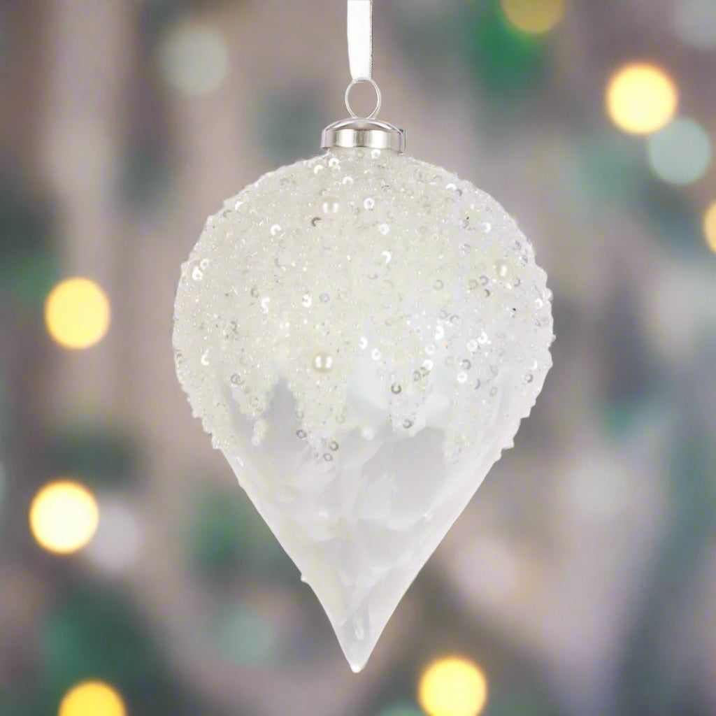 Decorative white teardrop ornament with sequins against a blurred festive background