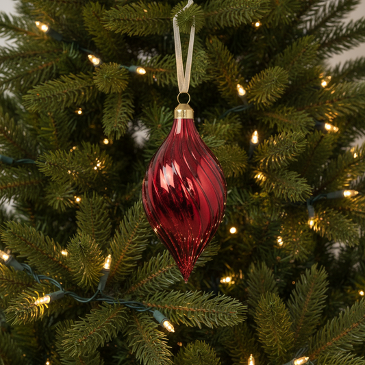 Red glass ornament hanging on a decorated Christmas tree with lights.