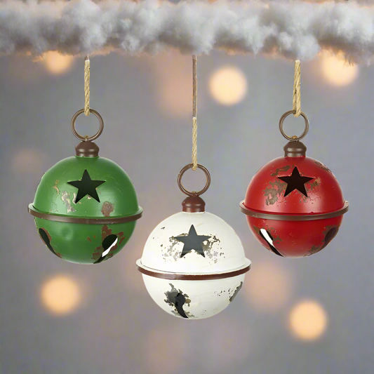 Three vintage style large metal Christmas bells with a star cut out design, in green, red, and white colors, hanging from rustic jute ropes.