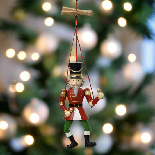Decorative nutcracker ornament hanging against a blurred Christmas tree background with lights.