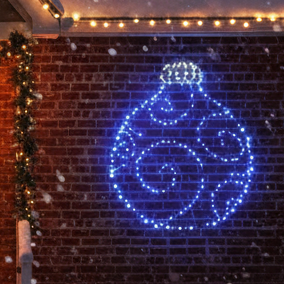 A blue and white LED Christmas bauble light string decoration twinkling on a dark brick wall.