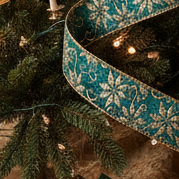 Decorated Christmas tree with lights, ornaments, and a blue ribbon in a room setting.